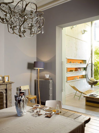 Salle à manger ouverte sur le salon déclinée dans une harmonie de gris, orange et de bois naturel pour un mélange de style cohérant. Peinture Astral