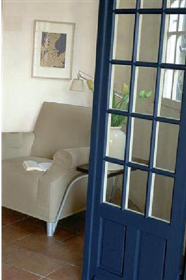 Une déco de salon travaillée en contraste de gris et blanc avec la peinture des murs et un fauteuil dans un doux ton de gris mastic. Le bleu intense de la peinture de la porte crée un joli contraste