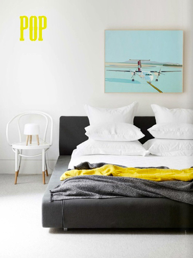 Un pochoir lettre POP réalisé avec une peinture jaune pour réveiller la peinture blanche d'une chambre adulte. En rappel, un plaid jaune en jeté sur un boutis gris anthracite