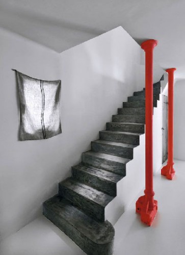 Soulignant l'architecture de la cage d'escalier grise et blanche, les marches peintes en gris anthracite et les 2 piliers rouge vif invitent à monter à l’étage sans précipitation pour profiter de l’ambiance épurée qui règne dans l’entrée.
